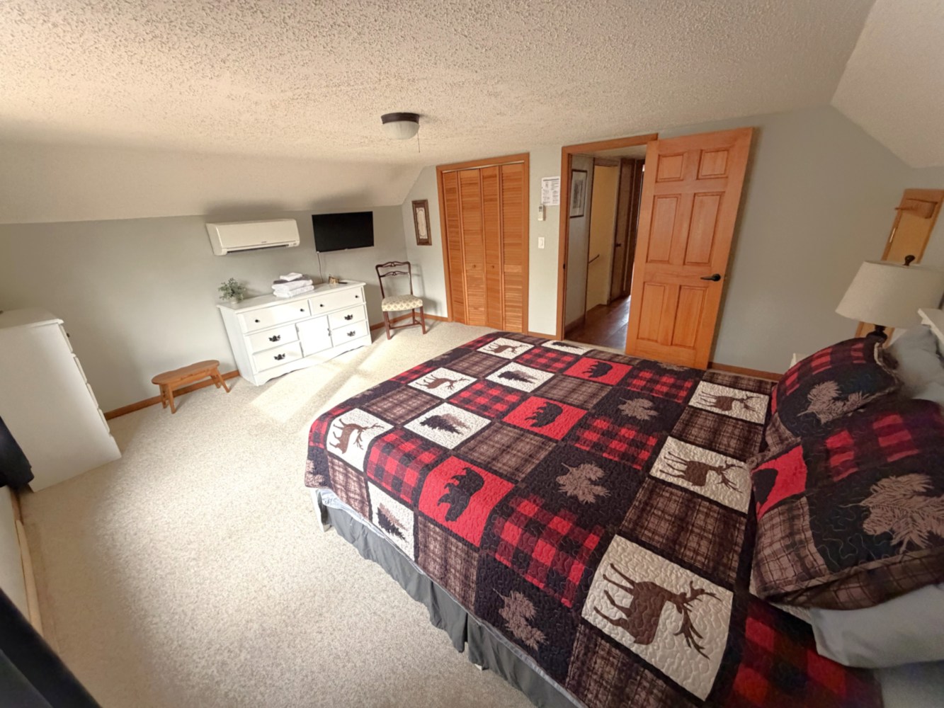 Cozy bedroom with patterned quilt, TV, dresser, and open wooden door.