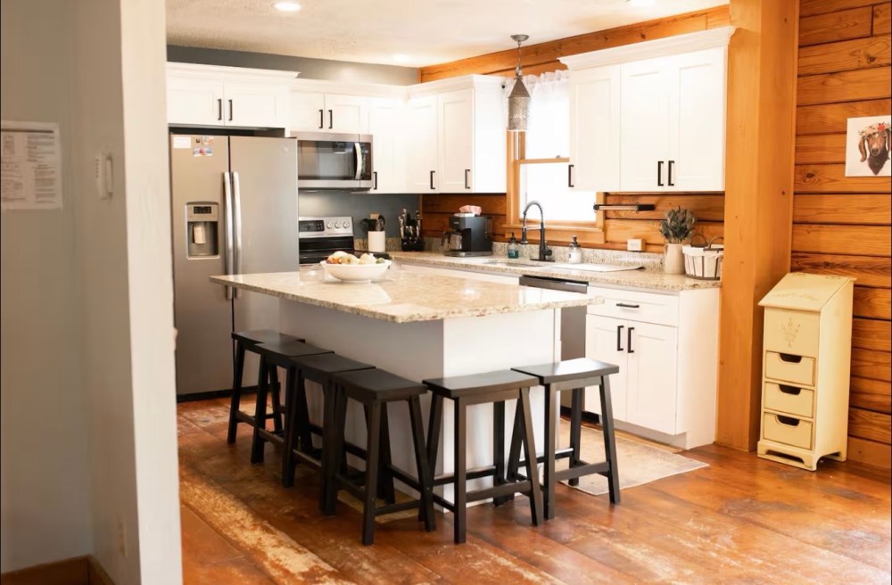 Cozy kitchen with wooden floors, white cabinets, island, and bar stools.